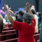 African American Woman Standing with Both Hands Raised in Church